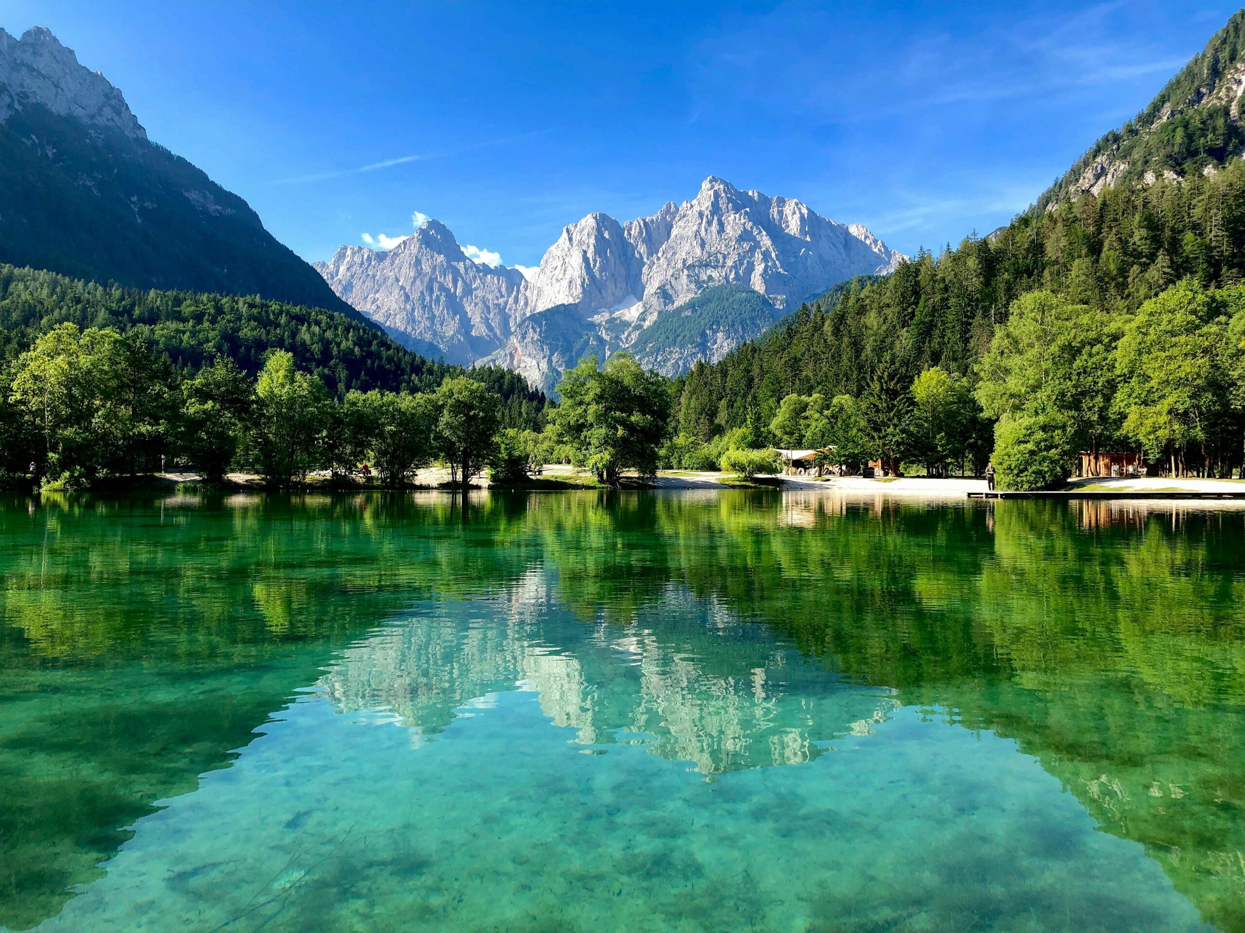 Serene landscape of Lake Jasna reflecting the Julian Alps under a clear blue sky in Slovenia.