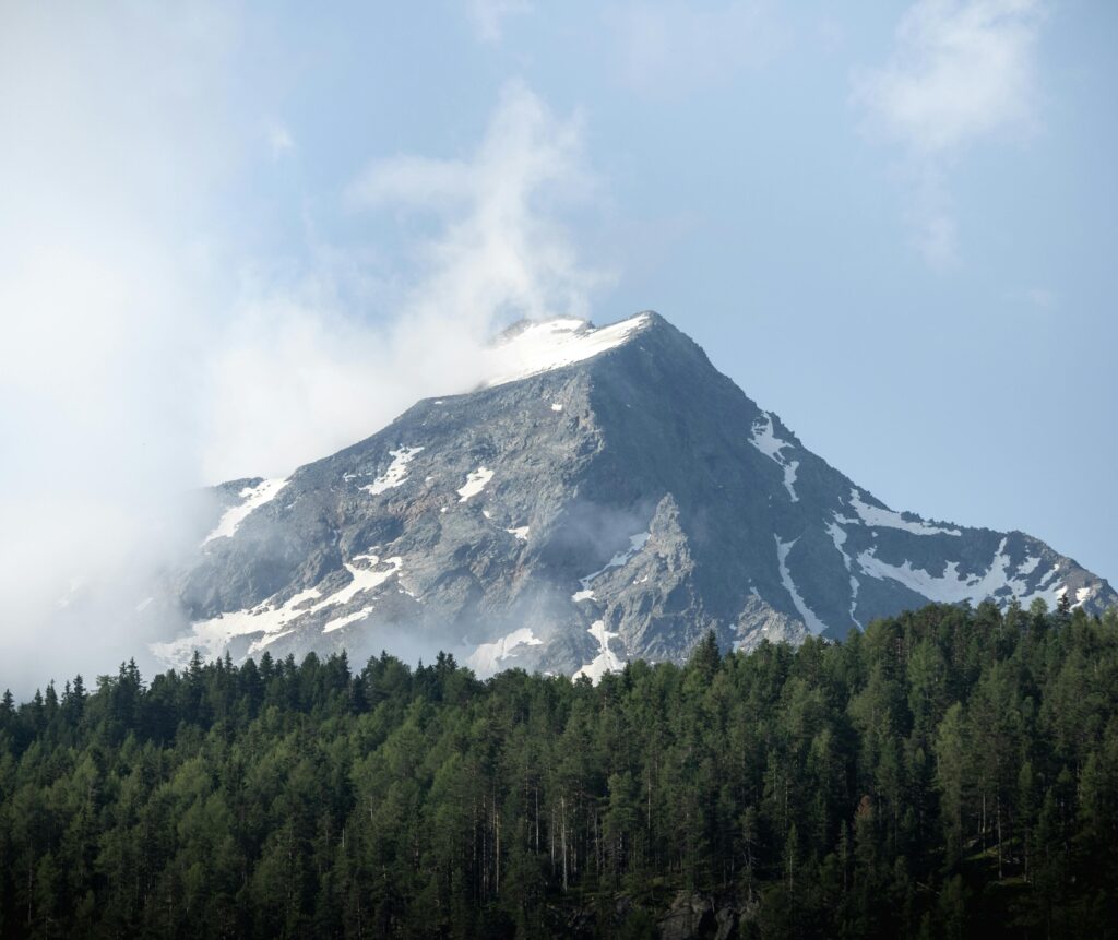 Stunning view of a snow-capped mountain peak surrounded by lush green forests in Sölden, Tirol.