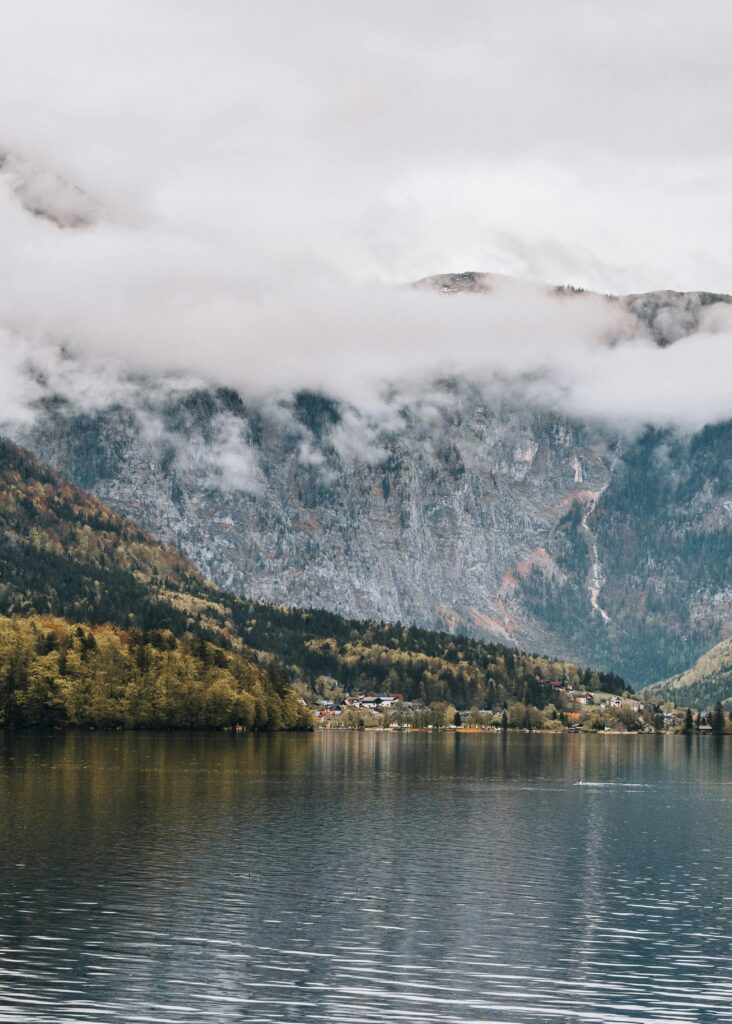 Calm waters reflect misty mountains and clouds in a serene alpine setting.